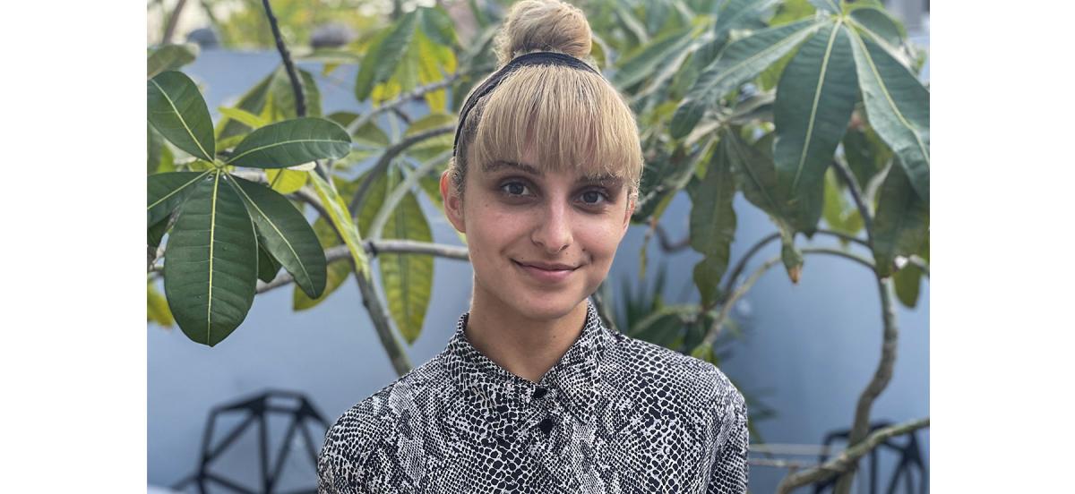 Karina smiles in a snakeskin-print button-down shirt in front of a large plant