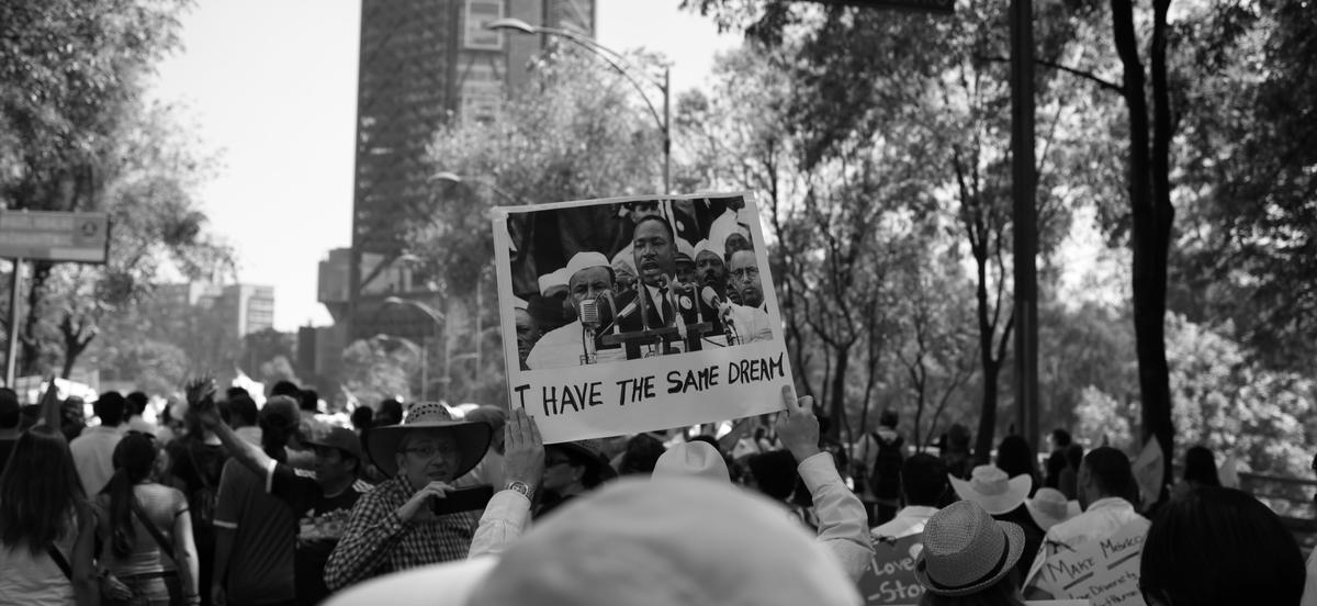 Person in crowd holds a sign aloft showing Marting Luther King Jr with the phrase I Have The Same Dream