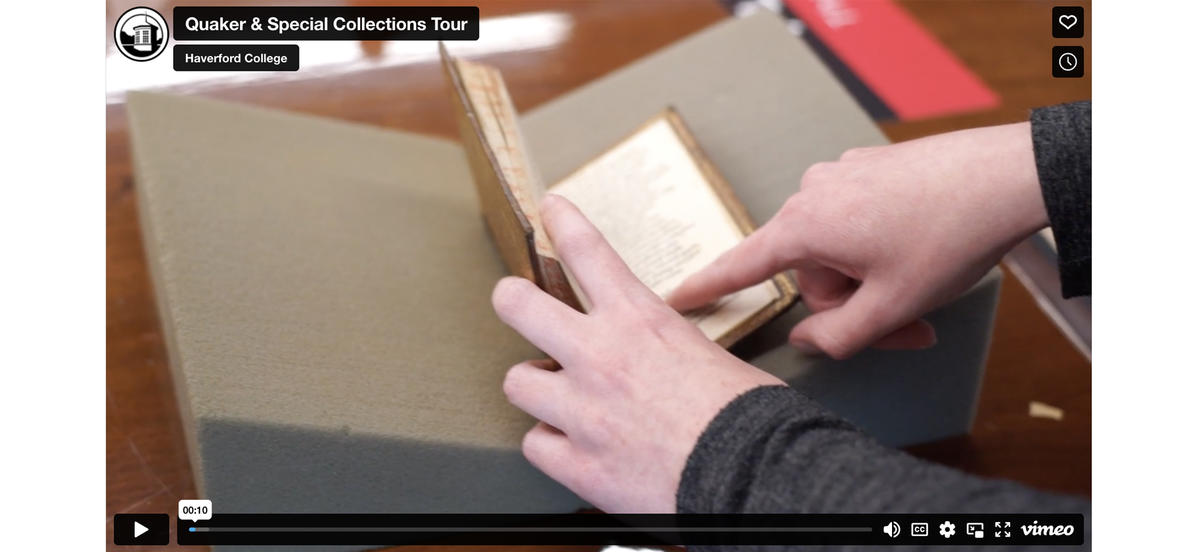 Video paused on two hands opening a small book and pointing inside