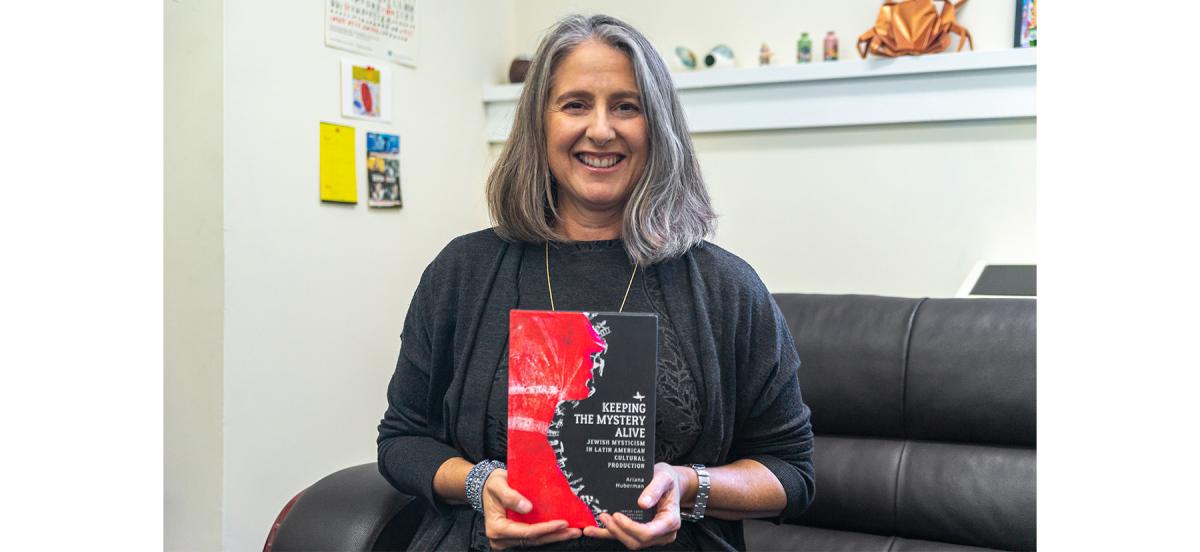 Photo of Spanish professor Ariana Huberman sitting and holding her new book, "Keeping the Mystery Alive: Jewish Mysticism in Latin American Cultural Production"