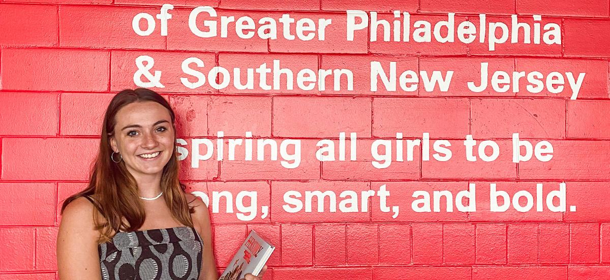A picture of Fiona in front of a pink wall with the words "of Great Philadelphia & Southern New Jersey inspiring all girls to be strong, smart, and bold."