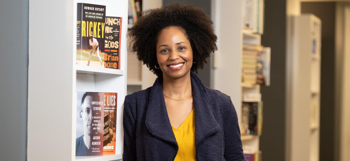 Rakia Clark '01 stands in front of a bookshelf, smiling.